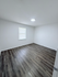 Bright, spacious room with stylish wood flooring and a modern ceiling light. A large window offers ample natural light, making it a perfect blank canvas for personalization.