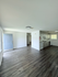 Bright and inviting open-concept living space with modern laminate flooring, featuring a spacious kitchen and natural light streaming through large windows.