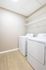 Modern laundry room with fresh white appliances and ample shelving.