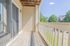 Bright and airy balcony with wooden decking, featuring elegant white railings and a view of lush green trees.
