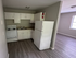 Contemporary kitchen with sleek white cabinets, modern appliances, and elegant wood flooring leading to a bright living area.