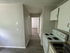 Modern apartment interior showcasing a streamlined kitchen with white cabinets, electric stove, and a view into a sunlit hallway with elegant wooden flooring.