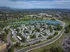Scenic aerial view of a modern apartment complex nestled amidst lush greenery and adjacent to a serene lake, offering a tranquil and picturesque living environment.