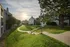 Serene apartment complex with lush green lawns, mature trees, and a charming walkway under a picturesque sunset sky.