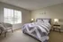 Cozy bedroom with modern d&eacute;cor, featuring a comfortable bed with chevron-patterned bedding, soft carpet flooring, natural light through large window with blinds, and contemporary side tables with stylish lamps.