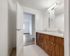 Bright and modern bathroom with dual sinks and sleek wood cabinetry, leading to a sunlit room with elegant wood flooring.
