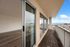 Spacious apartment balcony with stunning panoramic city and ocean views, featuring elegant wooden flooring and floor-to-ceiling glass doors.