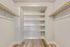 Bright and spacious walk-in closet with built-in shelving and modern wood flooring, offering ample storage and organization.