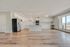 Beautiful open-concept kitchen with sleek white cabinetry, modern appliances, and expansive hardwood floors, bathed in natural light from large windows.