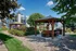 Charming outdoor communal area with a wooden gazebo, barbecue grill, and lush landscaping, perfect for entertaining.