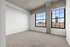 Bright and spacious room with large industrial-style windows, plush carpet flooring, and a stunning city skyline view.