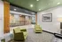 Charming modern lounge area with stylish green armchairs, exposed brick accent wall, and tasteful decor for a cozy ambiance.