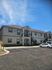 Inviting two-story apartment building with unique architectural detailing, surrounded by a spacious parking area under a clear blue sky.