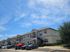 Modern two-story apartment complex with charming architectural details, ample parking, and a clear blue sky backdrop.