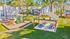 Charming residential complex surrounded by lush greenery featuring a modern playground and a stylish outdoor pavilion with picnic tables.