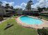 Inviting apartment complex with a sparkling swimming pool, sun loungers, and lush green surroundings under a clear blue sky.
