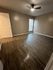 Inviting bedroom with sleek wooden flooring, chic neutral walls, and ample natural light from a tall window.