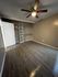 Spacious bedroom with sleek wooden flooring, modern ceiling fan, and ample open closet space.