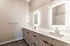 Modern bathroom with dual vanities, illuminated mirrors, and sleek wooden cabinetry.