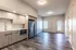 Modern kitchen with stainless steel appliances and sleek wood floor extending into a bright living area.