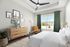 Bright and cozy bedroom with stylish decor, featuring a modern ceiling fan, textured dresser, and large window with green drapes illuminating the space.