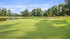 Picturesque golf course with lush green fairways, serene pond, and vibrant trees under a clear blue sky.