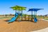 Vibrant playground with blue and green slides, colorful climbing structures, and sunshade canopies in a scenic park setting.