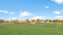 Expansive grassy field with a clear blue sky and nearby residential homes, perfect for outdoor activities and relaxation.