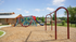 Inviting community playground featuring swings, climbing nets, and a slide, set against a backdrop of lush greenery and cozy homes.