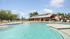 Luxurious outdoor pool with surrounding lounge chairs and a modern clubhouse under a clear blue sky.