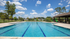 Inviting outdoor swimming pool under a clear blue sky, surrounded by lush greenery and vibrant playground area.