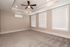 Spacious carpeted room with elegant tray ceiling and ceiling fan, featuring large windows with white blinds for ample natural light.