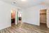 Bright empty room featuring elegant hardwood floors, an open walk-in closet, and doorway leading to a modern bathroom with sleek countertops.