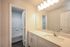 Bright and modern bathroom with elegant vanity, large mirror, and sleek fixtures adjacent to a tiled bathtub.