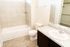 Bright and modern bathroom featuring a sleek sink vanity, large mirror, tiled bathtub area, and elegant flooring.
