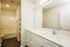 Bright and modern bathroom with sleek countertop, large mirror, built-in shelving, and bathtub with shower.