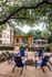 Charming outdoor seating area with blue chairs around a fire pit, surrounded by lush greenery and a stylish pergola near a modern apartment complex.