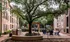 Serene apartment courtyard featuring mature trees, communal seating, and a BBQ area surrounded by elegant brick architecture.