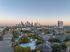 Stunning aerial view of a vibrant apartment complex with a sparkling pool, set against a breathtaking city skyline at sunset.