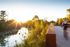 Serene riverside scene with vibrant foliage, a glowing sunset, and active pathways perfect for biking and scenic walks.