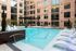 Chic urban apartment complex featuring a sparkling swimming pool, elegant lounge chairs, and lush landscaping against a backdrop of stylish brick architecture.
