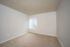 Bright empty room with plush carpet and a window with vertical blinds.