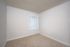 Bright and empty room with soft beige carpeting and a large window with vertical blinds.