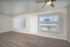 Sunlit living room with large windows, wooden flooring, and ceiling fan.