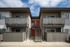 Inviting apartment exterior with modern dual-level balconies and bold red doors, under a clear blue sky.