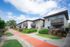 Charming apartment complex with balconies, lush landscaping, and a vibrant walkway under a bright blue sky.