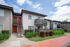 Modern two-story apartment complex with red doors and private balconies, surrounded by well-maintained gardens and a vibrant walkway.