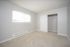 Bright, empty bedroom with fresh carpeting, large closet, and natural light streaming through vertical blinds.
