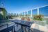 Chic rooftop terrace with modern seating, lush greenery, and panoramic city views under a clear blue sky.