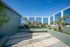 Charming rooftop terrace with lush greenery, vibrant planters, and expansive glass views under a clear blue sky.